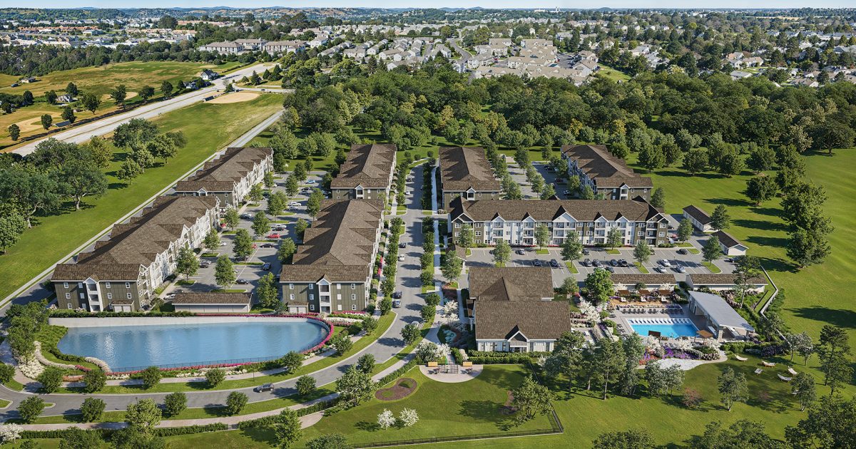 Aerial view of apartment community with lake, clubhouse, and landscaped grounds